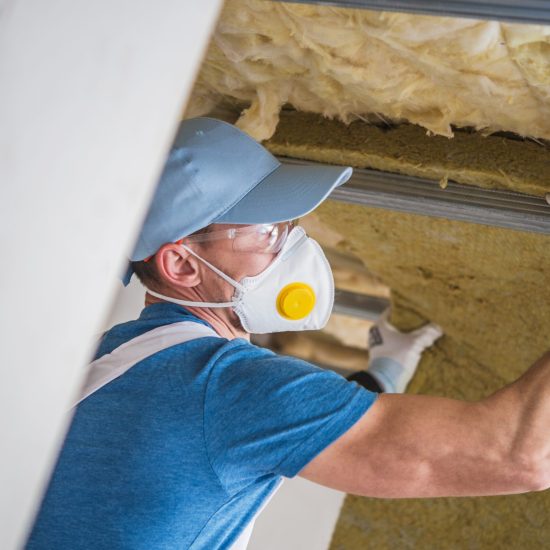 Mineral Wool Insulation by Professional Insulating Worker. Caucasian Construction Worker in His 30s.
