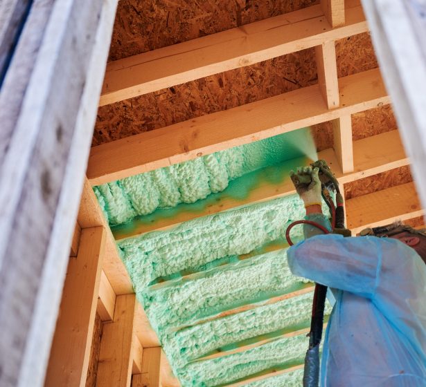 Male builder insulating wooden frame house. Man worker spraying polyurethane foam inside of future cottage, using plural component gun. Construction and insulation concept.